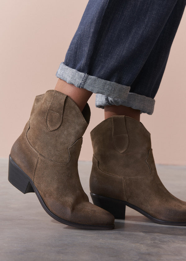 Brown suede ankle boots worn with rolled-up jeans on a neutral background