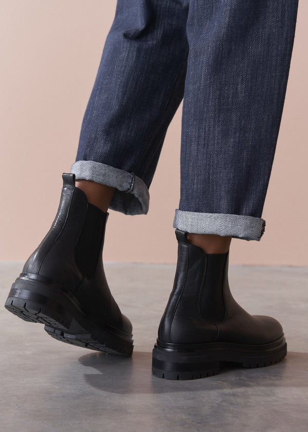 Black rubber boots worn with rolled-up jeans on a neutral background