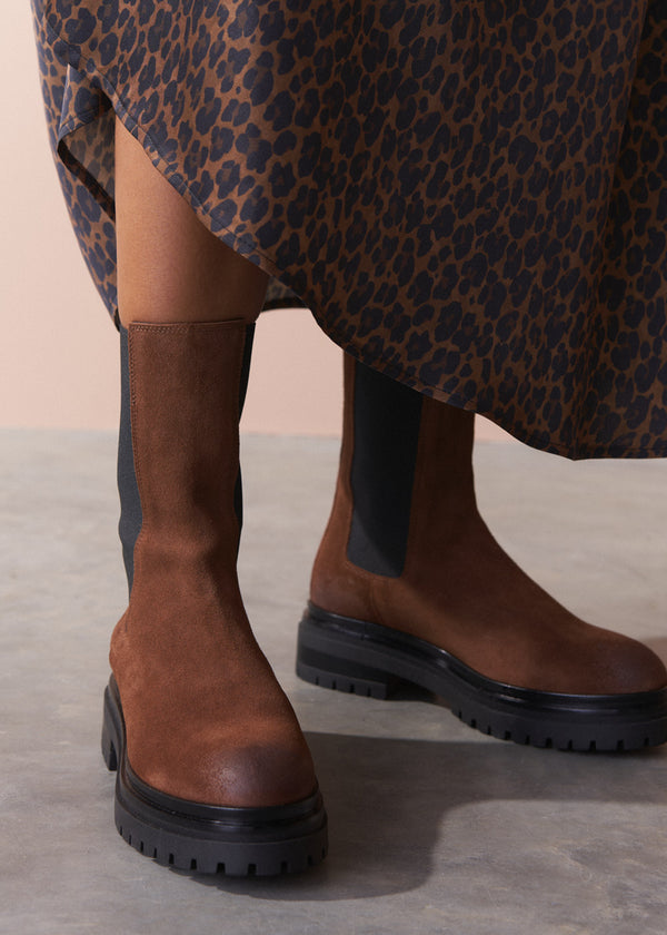 Brown knee-high boots worn with a leopard print skirt on a neutral background
