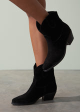Black suede ankle boots worn by a person on a neutral background