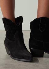 Black suede cowboy boots worn by a person on a neutral background