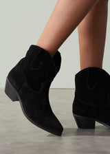 Black suede ankle boots worn by a person on a neutral background