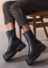Person wearing black platform boots with leopard print trousers sitting on a chair.