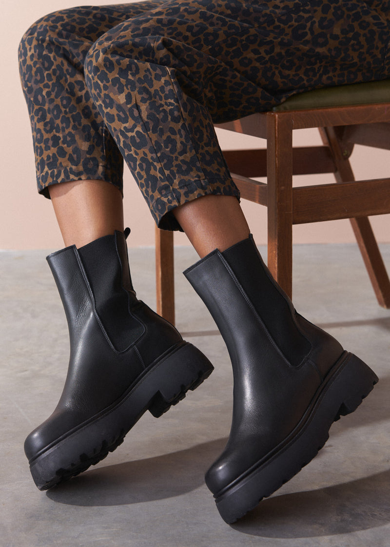Person wearing black platform boots with leopard print trousers sitting on a chair.