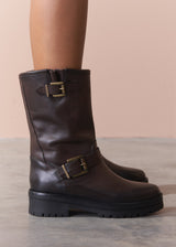 Brown leather boots with gold buckles on a neutral background