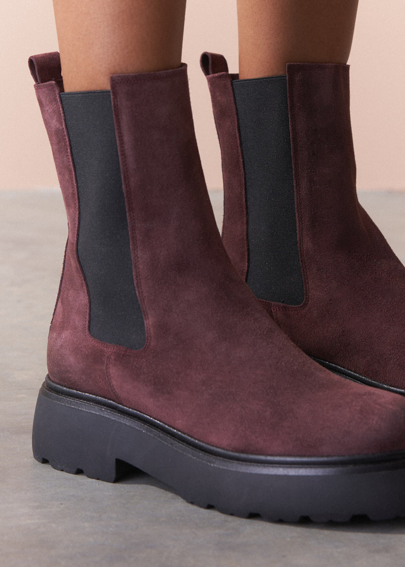 Burgundy suede boots with black elastic sides on a neutral background