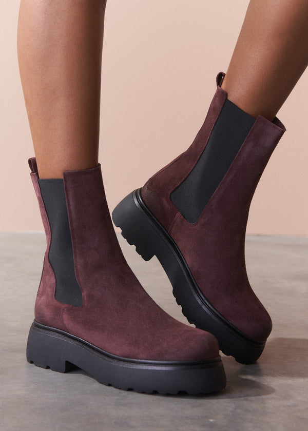 Burgundy Chelsea boots with black accents worn by a person on a neutral background