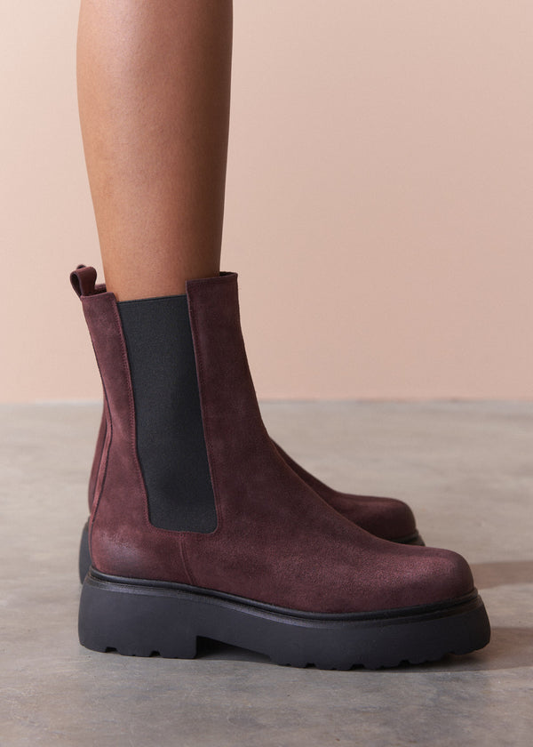 Burgundy suede boots with black soles on a neutral background