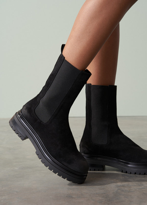 Black Chelsea boots worn by a person on a neutral background