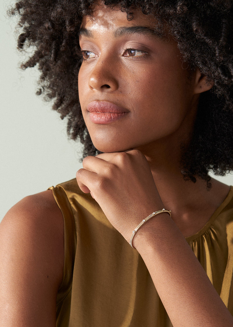 Woman wearing a gold sleeveless top and bracelet against a light background