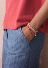 Person wearing a red shirt and blue jeans with a bracelet on a neutral background