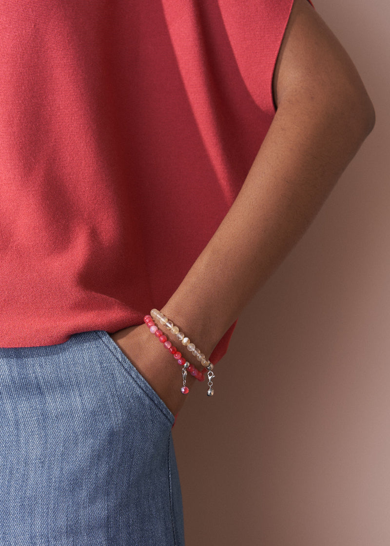 Person wearing a red sleeveless top and blue jeans with a bracelet on a brown background