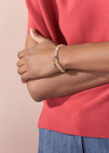 Person wearing a red shirt and blue pants with a bracelet on a beige background