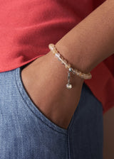 Close-up of a wrist wearing a beaded bracelet with a red shirt and blue jeans in the background.