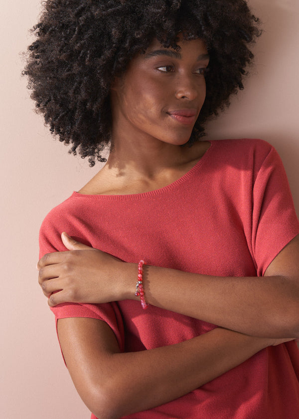 Woman wearing a red top and red bead bracelet against a beige background