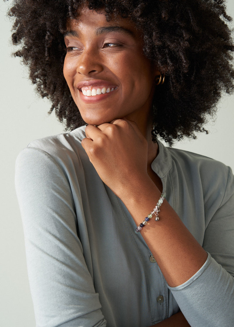 Woman wearing a light gray shirt and a bracelet, smiling against a neutral background