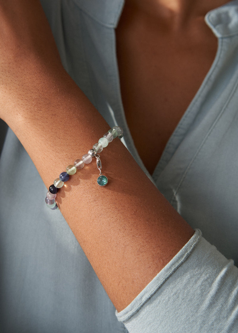 Close-up of a wrist wearing a bracelet with colorful beads against a light gray background.