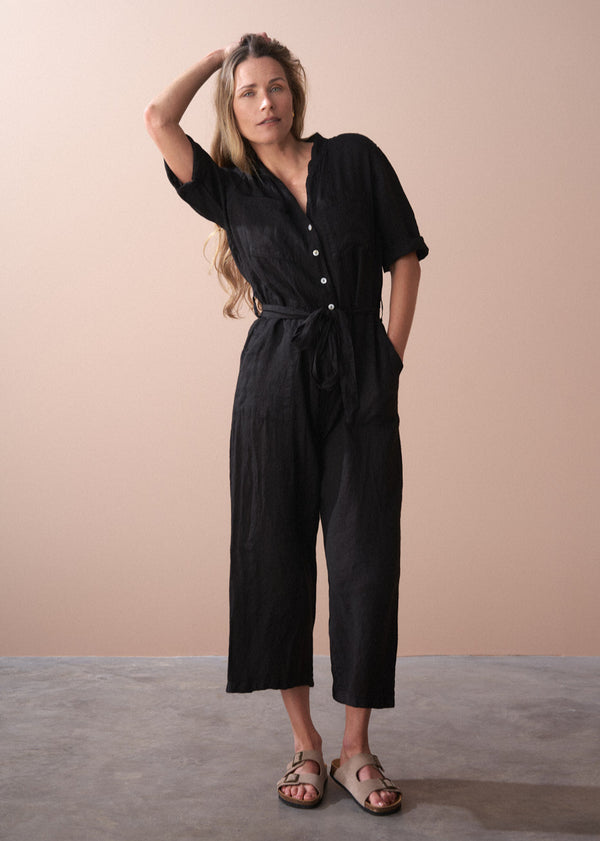 Woman wearing a black linen jumpsuit against a beige background