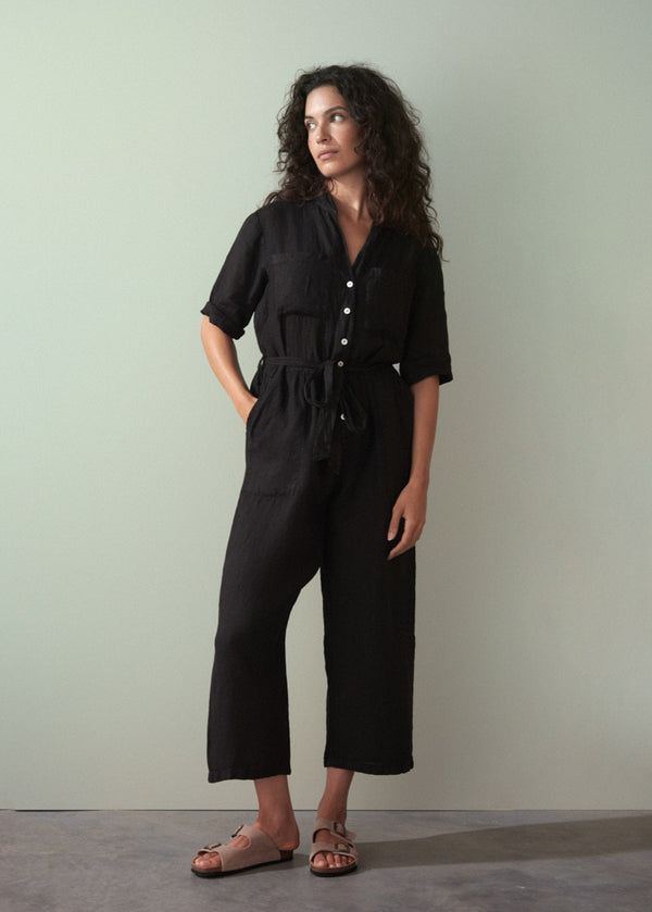 Woman wearing a black linen jumpsuit against a plain background