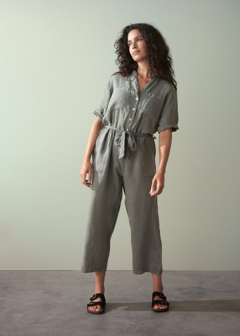 Woman wearing a khaki green linen jumpsuit against a plain background