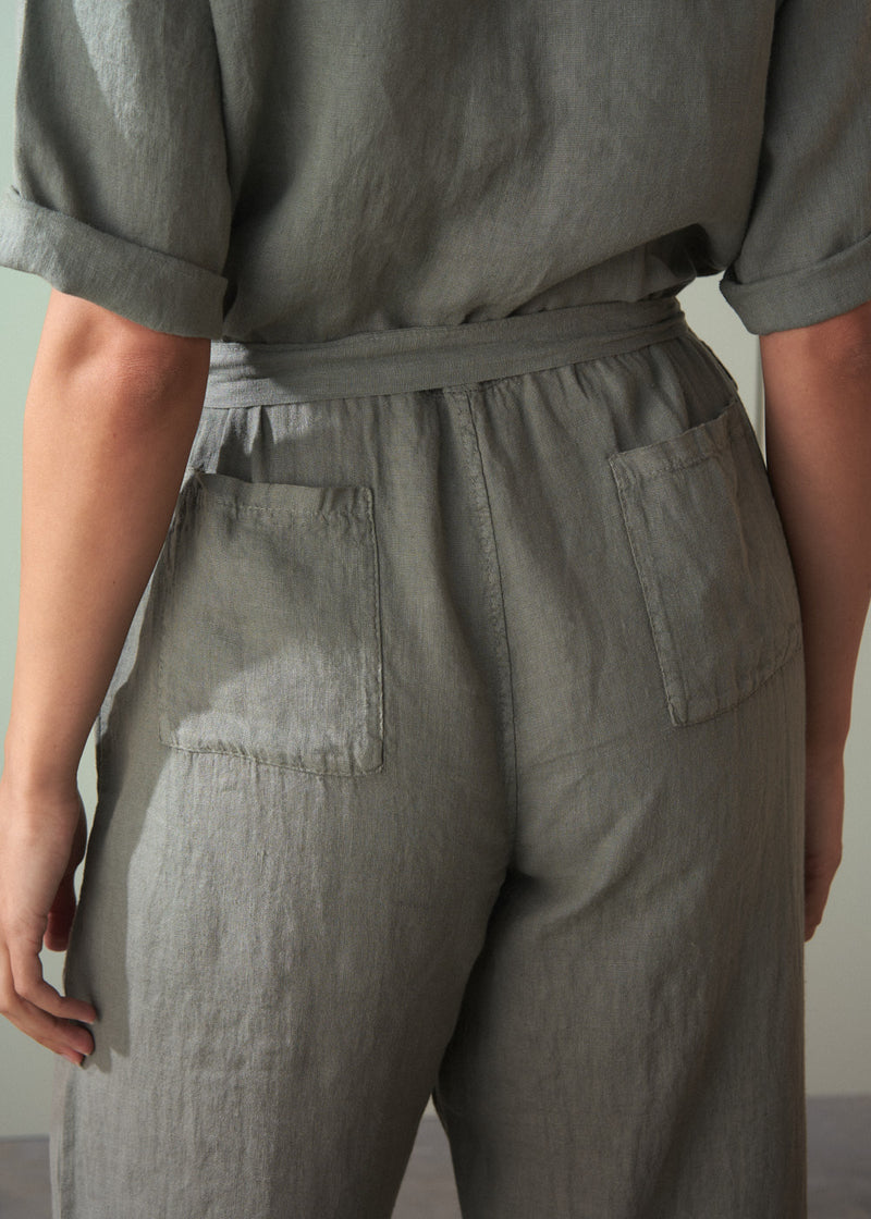 Person wearing a khaki green linen jumpsuit with a belt against a neutral background