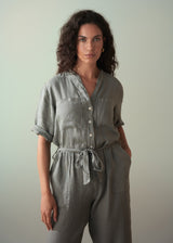 Woman wearing a khaki green linen jumpsuit against a plain background