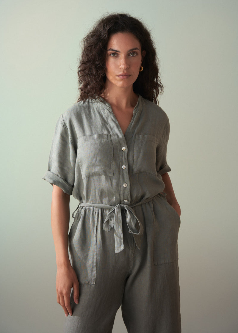 Woman wearing a khaki green linen jumpsuit against a plain background