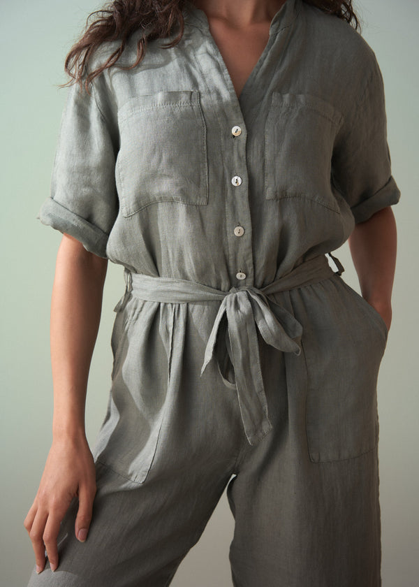 Person wearing a khaki green linen jumpsuit against a plain background