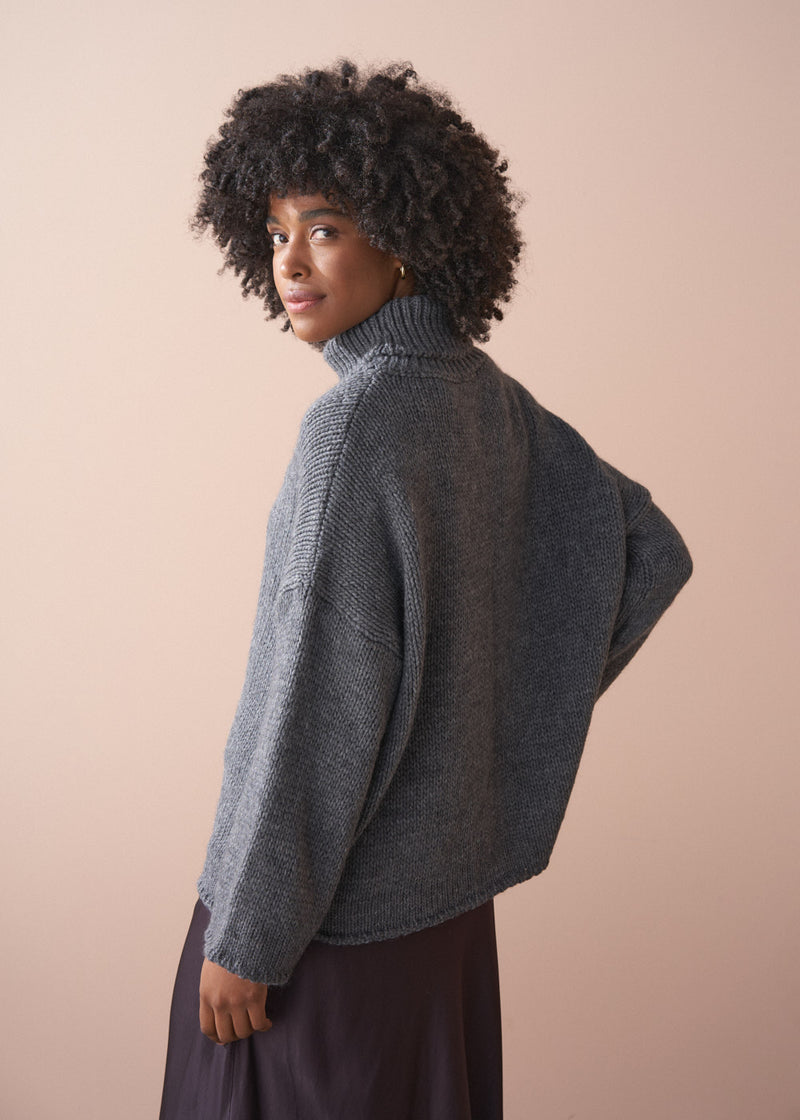 Person wearing a grey chunky knit sweater and satin bias cut skirt against a beige background