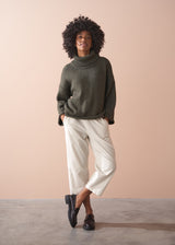 Woman wearing a green chunky knit toll neck sweater and oatmeal cord trousers against a beige background