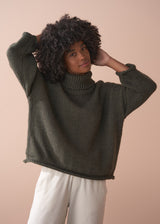 Woman wearing a green chunky knit toll neck sweater and oatmeal cord trousers against a beige background
