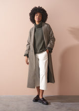 Woman wearing a green chunky knit toll neck sweater and oatmeal cord trousers against a beige background