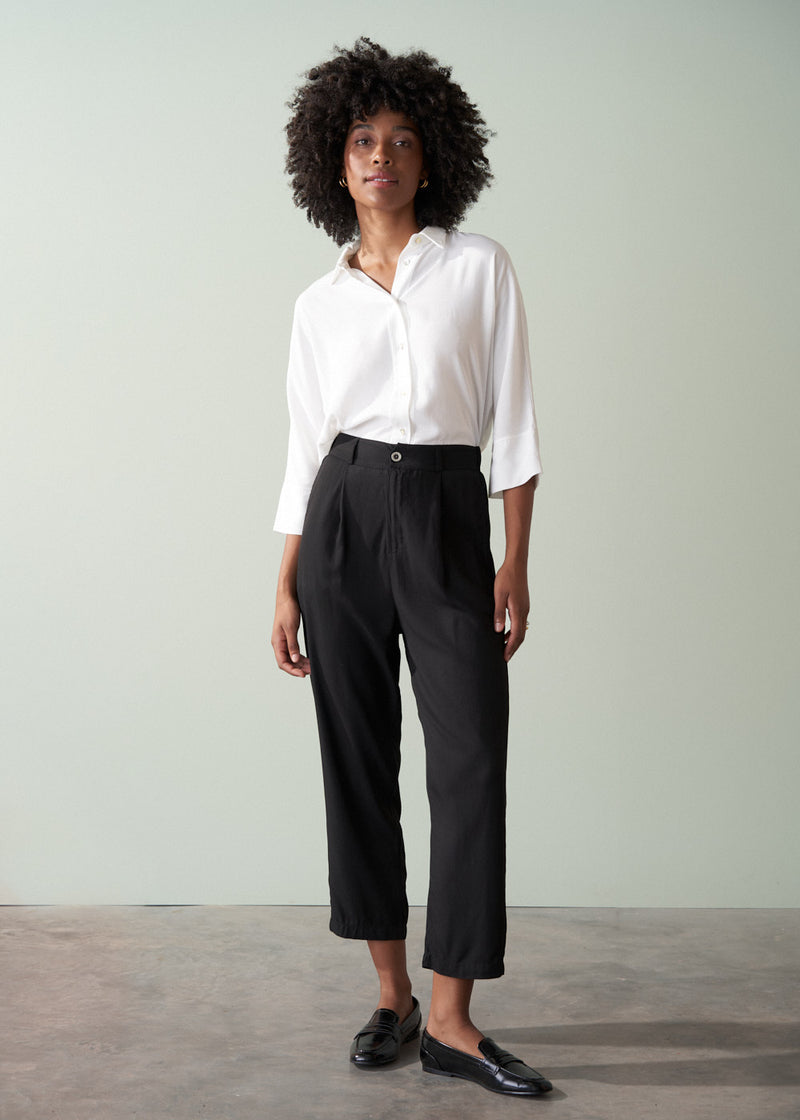 Person wearing a white shirt and black tapered trousers against a plain background