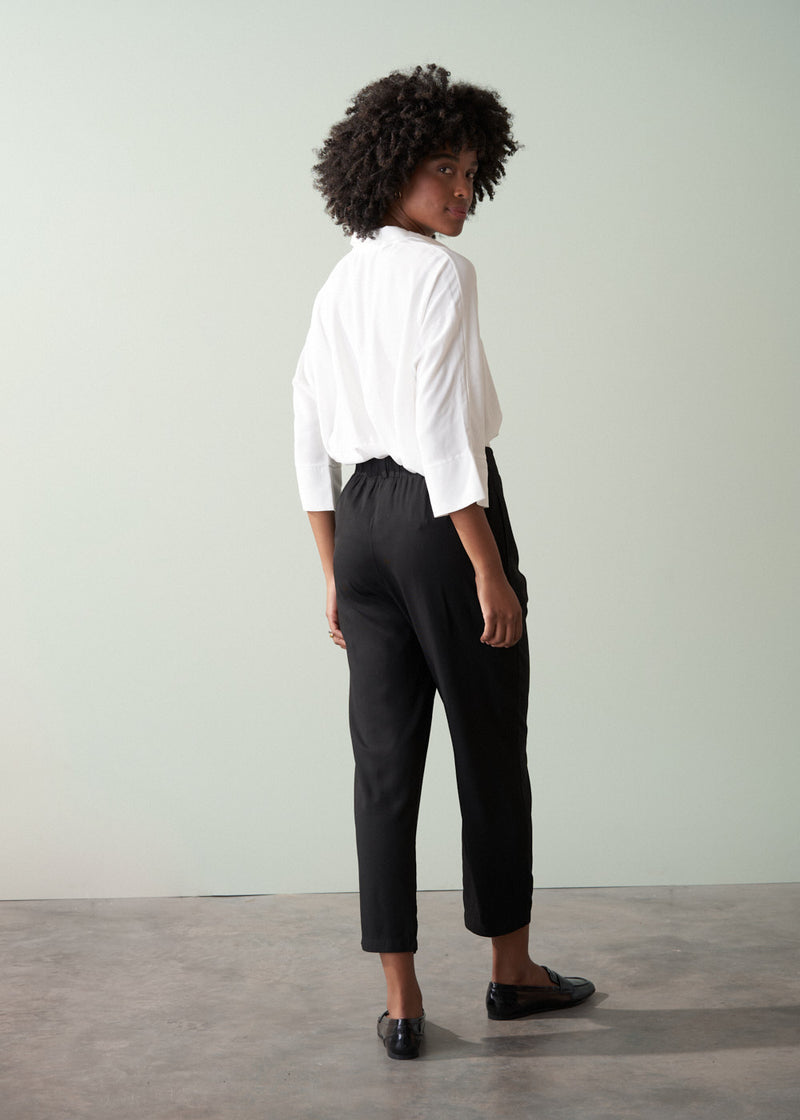 Person wearing a white shirt and black tapered trousers against a plain background