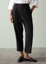 Person wearing a white shirt and black tapered trousers against a plain background