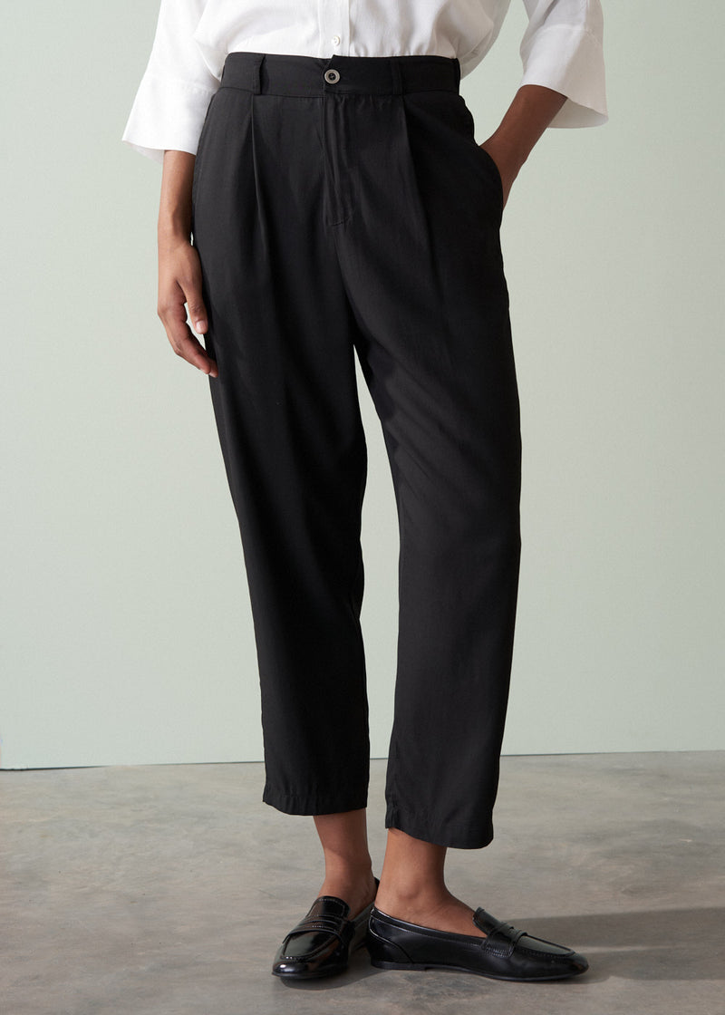 Person wearing a white shirt and black tapered trousers against a plain background