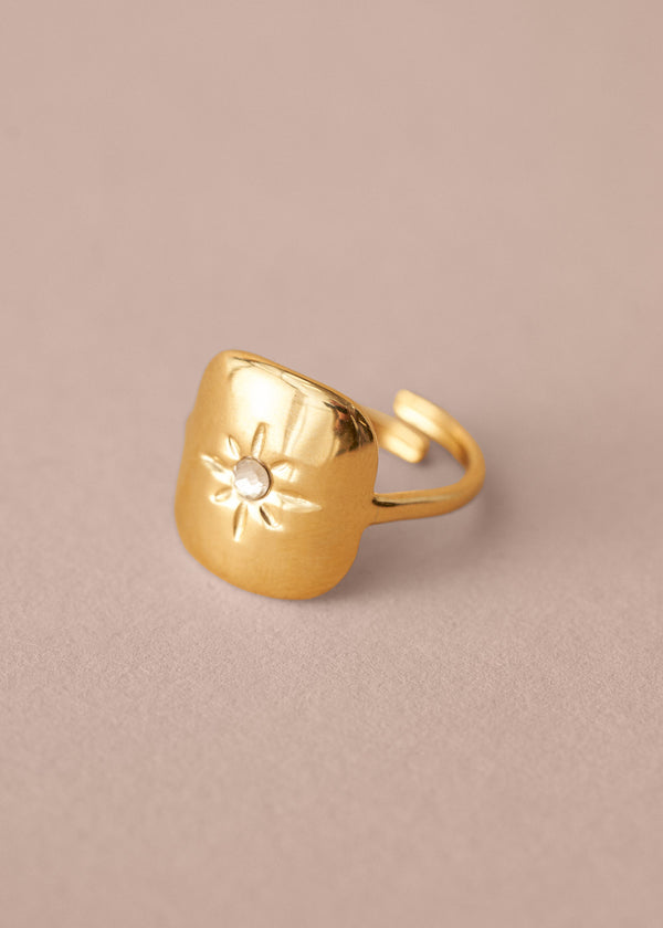 Gold ring with a sun design on a beige background