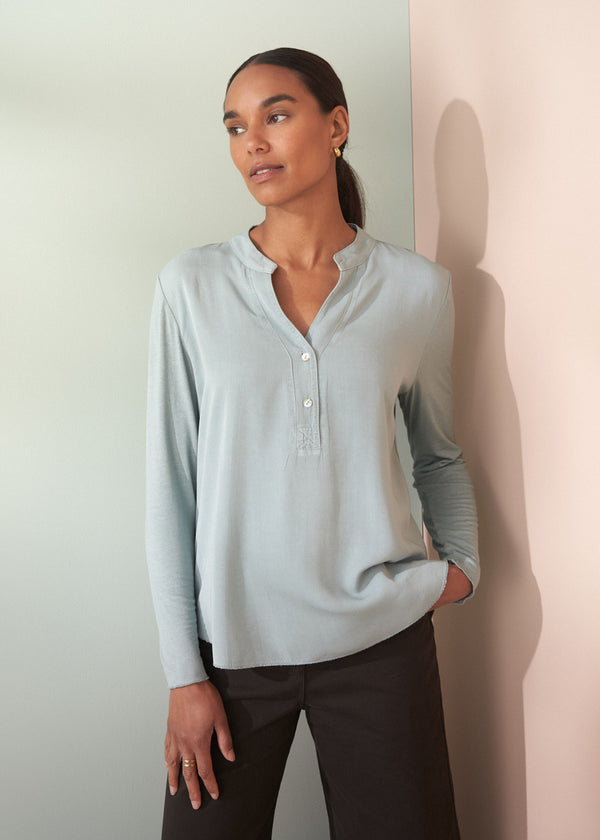 Woman wearing a light blue long-sleeve shirt against a plain background