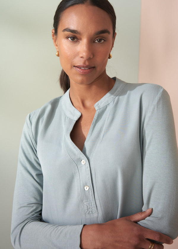 Woman wearing a light blue long-sleeve shirt against a neutral background