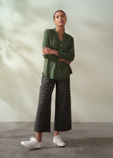 Woman wearing a green shirt and patterned pants standing against a plain background