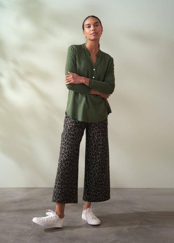 Woman wearing a green shirt and patterned pants standing against a plain background
