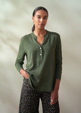 Woman wearing a green long-sleeve shirt and patterned pants against a plain background