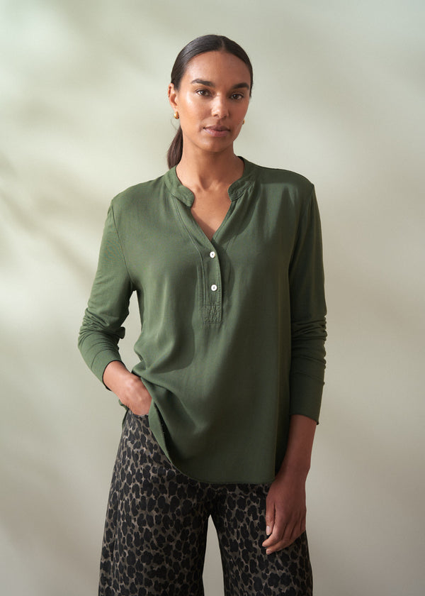 Woman wearing a green long-sleeve shirt and patterned pants against a plain background