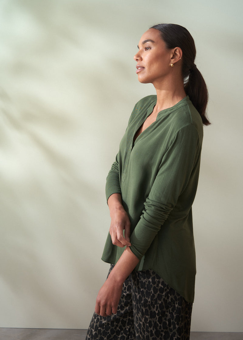 Woman wearing a green long sleeve top against a plain background