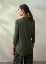 Woman wearing a green long-sleeve top and patterned pants against a neutral background