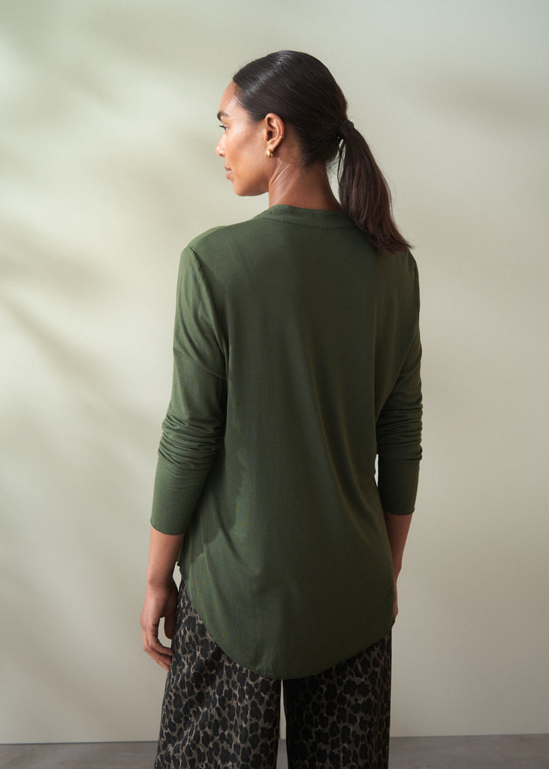 Woman wearing a green long-sleeve top and patterned pants against a neutral background