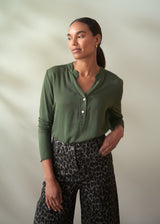 Woman wearing a green shirt and patterned pants against a plain background