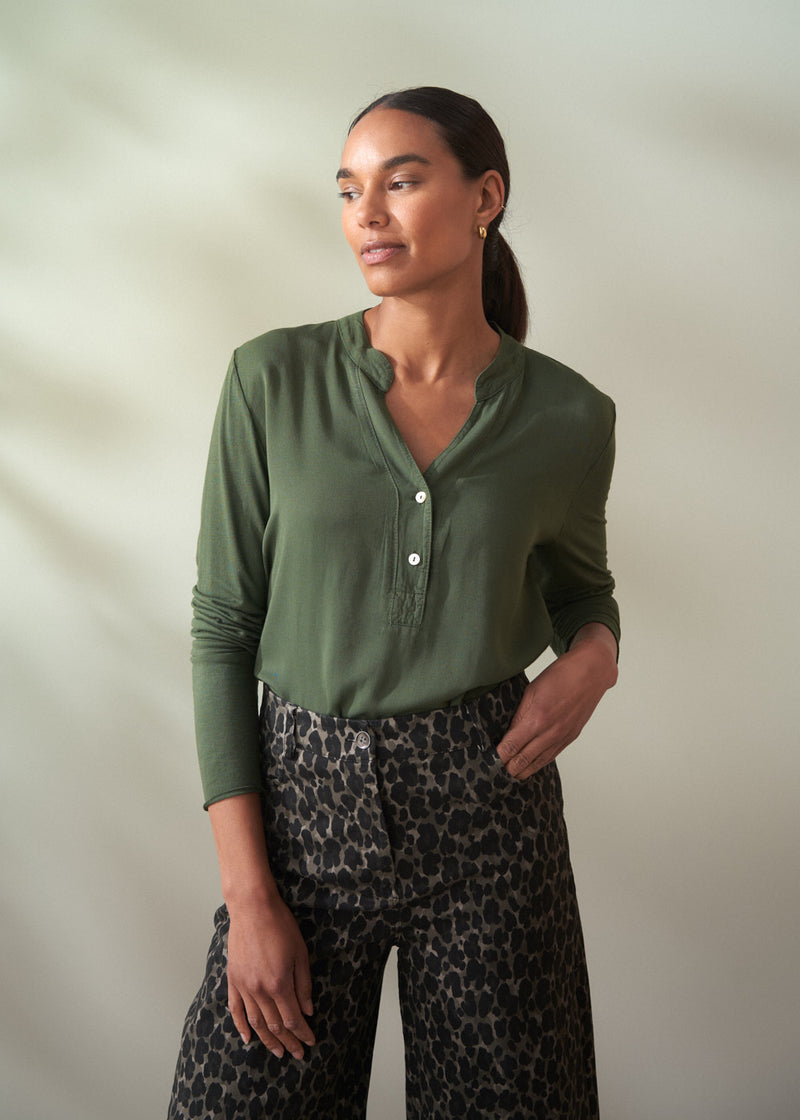 Woman wearing a green shirt and patterned pants against a plain background