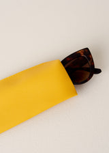 Brown tortoiseshell sunglasses in yellow neoprene case on beige background