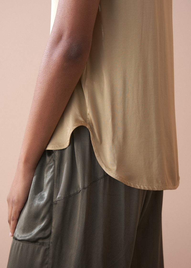 Woman wearing a light yellow satin blouse and green satin trousers against a beige background